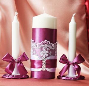 white pillar candle and white taper candles with purple ribbons 