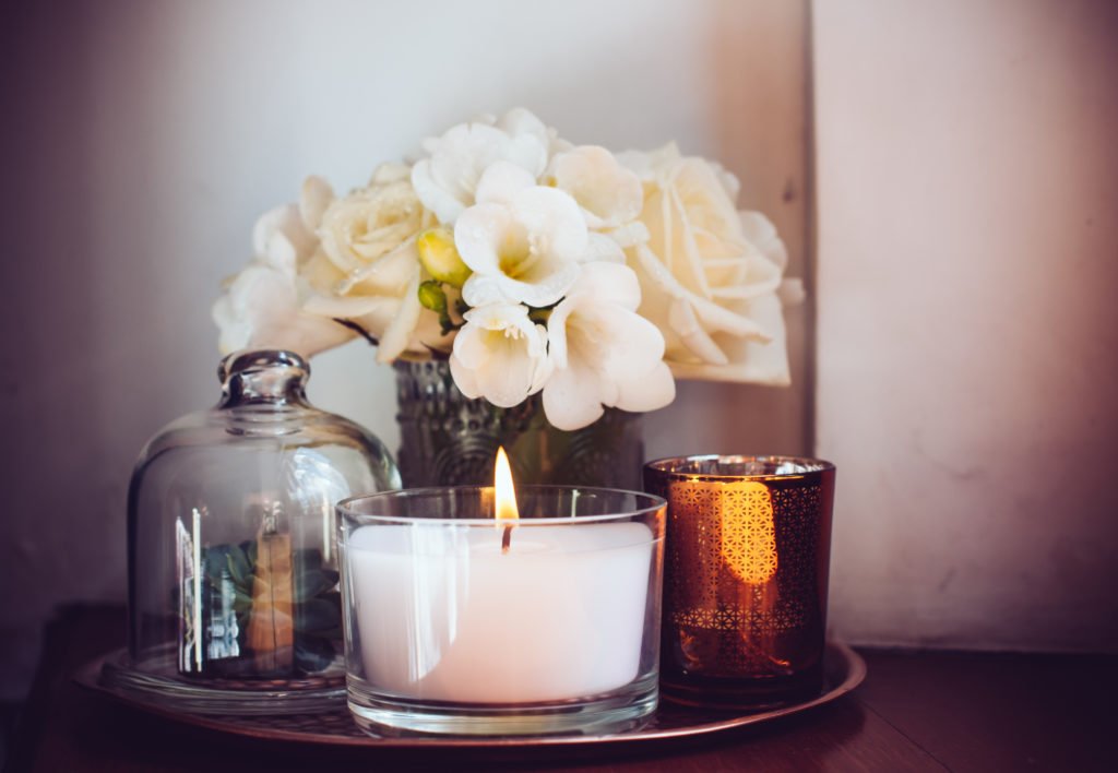 burning home candle in jar on tray with white flowers