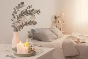 burning candles and eucalyptus in vase in white bedroom