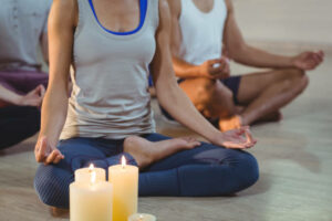 Group of people performing yoga in fitness studio with pillar candles 